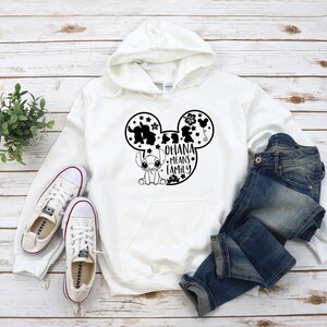 K&ouml;nnte beinhalten: Wei&szlig;er Hoodie mit einer schwarzen Mickey-Maus-Silhouette und dem Text "Ohana means family" in den Ohren. Stitch befindet sich unten in der Mickey-Maus-Silhouette.