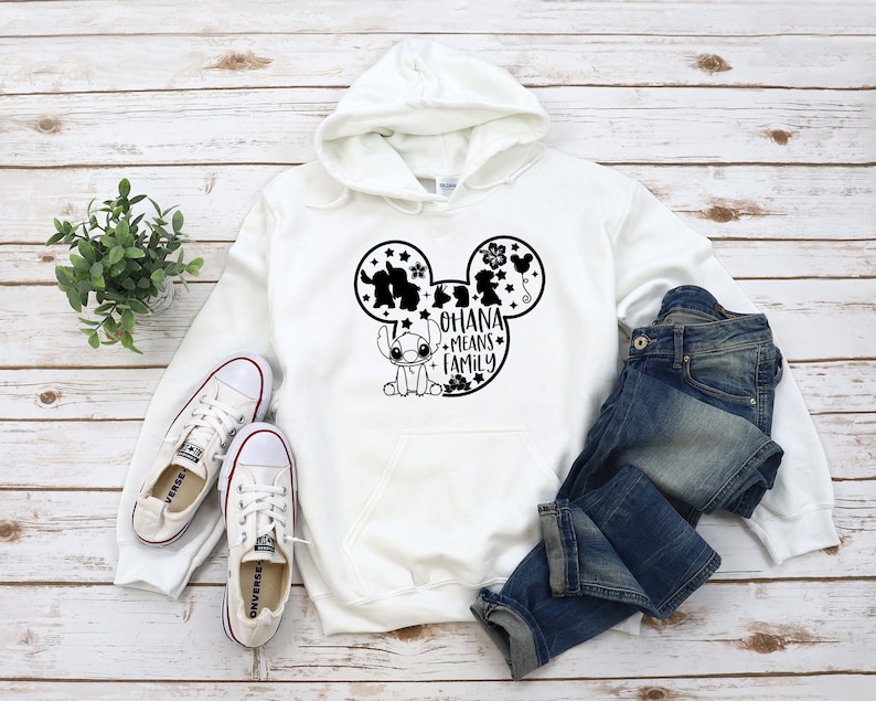 K&ouml;nnte beinhalten: Wei&szlig;er Hoodie mit einer schwarzen Mickey-Maus-Silhouette und dem Text "Ohana means family" in den Ohren. Stitch befindet sich unten in der Mickey-Maus-Silhouette.