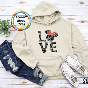 May include: A beige hoodie with a black and white graphic of Mickey Mouse heads forming the word "LOVE". The graphic also includes a red bow on top of a Mickey Mouse head.