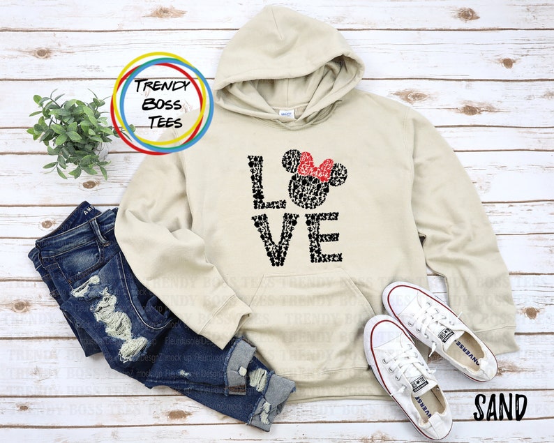 May include: A beige hoodie with a black and white graphic of Mickey Mouse heads forming the word "LOVE". The graphic also includes a red bow on top of a Mickey Mouse head.