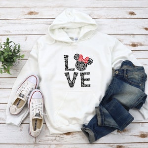 May include: White hooded sweatshirt with a black and white graphic of Mickey Mouse heads forming the word "LOVE" with a red bow on the top of the "O".