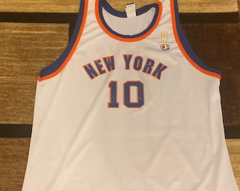 May include: White basketball jersey with blue and orange trim. The jersey has "NEW YORK" written across the chest in orange and blue lettering with the number "10" underneath. The Champion logo is on the upper right side of the jersey. The jersey is size 52.