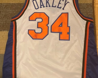 May include: White basketball jersey with blue and black trim. The back of the jersey has the name "OAKLEY" and the number "34" in orange.