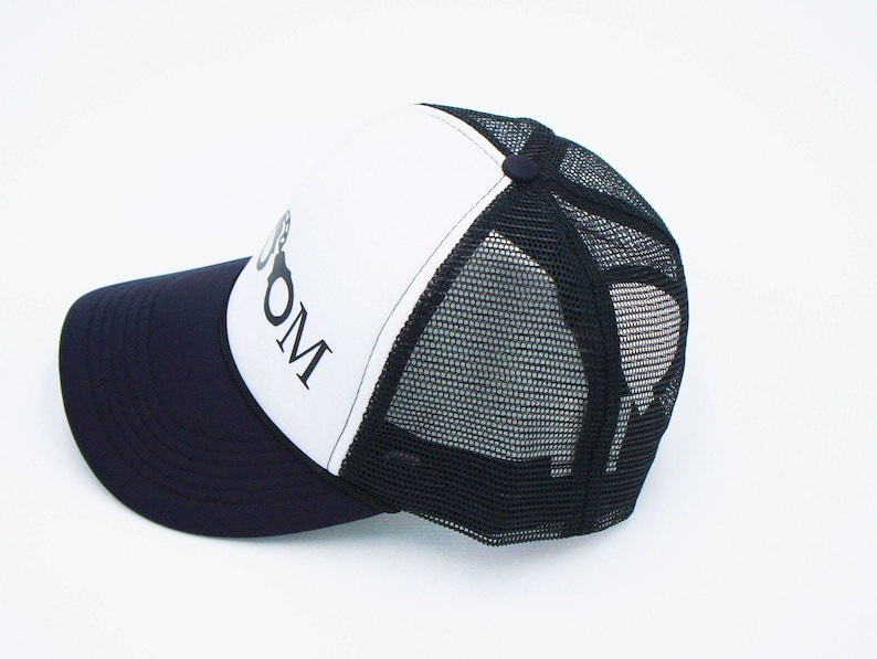 May include: A white and black trucker hat with a black mesh back. The front of the hat has a black and white logo that says "BOOM".