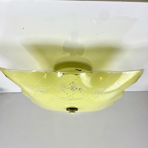May include: A vintage ceiling light fitting with a yellow-tinted glass shade. The shade features a decorative floral and geometric pattern. The fitting has a brass-coloured base and a scalloped edge. Designed to be mounted flush against the ceiling.