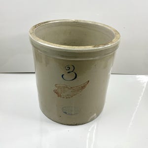 Peut inclure: Un pot en grès vintage avec un glaçage beige. Le pot présente le chiffre bleu "3" et un motif d'aile marron. Un petit tampon circulaire est visible en bas. Le récipient cylindrique a une large ouverture et est probablement utilisé pour le stockage.