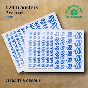 Pode incluir: Três folhas de transferências de vinil pré-cortadas azuis com um design de cobra. As folhas são etiquetadas com "174 transferências", "Pré-cortadas", "Azul", "www.forgottenchapters.eu" e "#IBST036".