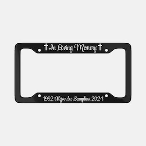 May include: Black metal license plate frame with white text that reads "In Loving Memory + 1992 Alejandro Sampilna 2024".