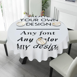 May include: A white round tablecloth with black text reading "CREATE YOUR OWN DESIGN" and "Any font, Any colour, Any design." The tablecloth is on a black table with white chairs. Gold cutlery is on small white plates.