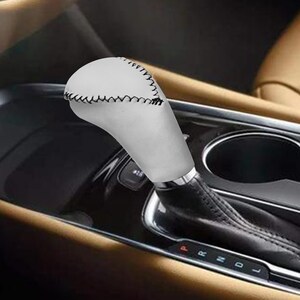 Puede incluir: Una palanca de cambios de cuero blanco con costuras negras. La palanca est&aacute; unida a una palanca de cambios negra. La palanca de cambios est&aacute; en un coche.