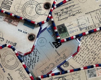 Puede incluir: Un conjunto de etiquetas de tela de estilo vintage con temática de postales. Las etiquetas presentan diseños impresos de postales antiguas, sellos y mensajes manuscritos. Cada etiqueta está bordeada con costuras rojas, blancas y azules y tiene un ojal metálico.