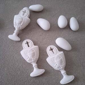 Può includere: Favori di comunione in ceramica bianca a forma di calice con una croce e le lettere "JHS" sul davanti. I calici sono circondati da confetti bianchi a forma di mandorla.