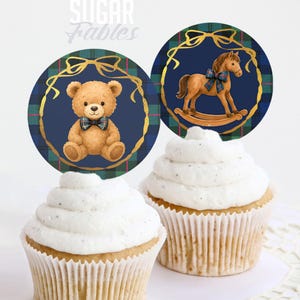 Puede incluir: Dos cupcakes cubiertos con glaseado blanco, cada uno adornado con un adorno circular. Uno presenta un oso de peluche con pajarita a cuadros, el otro un caballito balanc&iacute;n. Ambos sobre un fondo azul marino con marco dorado y detalles a cuadros. El texto "Sugar Fables" est&aacute; en la parte superior.