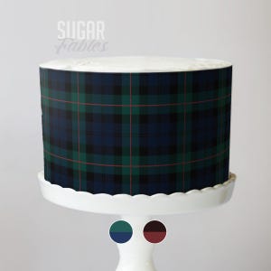 May include: A round cake with a navy blue, green, and red plaid pattern. The cake sits on a white scalloped cake stand. The text "Sugar Fables" is in the upper left corner.