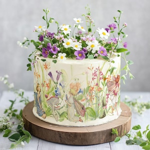 edible cake wrap features a delicate, hand-painted botanical illustration with fairies nestled among lush flowers, leaves, and mushrooms. The intricate artwork includes pastel tones with vibrant floral accents, evoking a whimsical, storybook-inspired aesthetic.