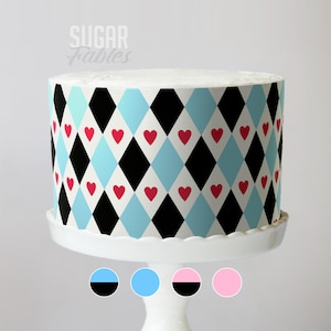 May include: A round cake with a white top and a patterned exterior. The pattern features black and light blue diamonds with red heart accents. The cake sits on a white cake stand. The text "Sugar Fables" is visible.