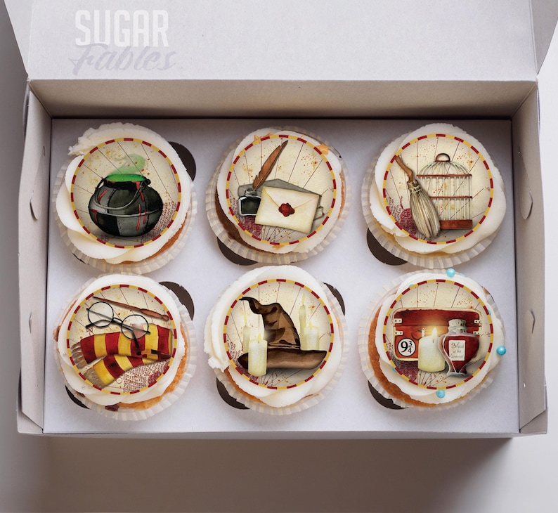 A box containing six cupcakes decorated with various Harry Potter-themed items, including a wand, a wand-like object, a wand-like hat, a wand-like book, a wand-like broom, and a wand-like cauldron.