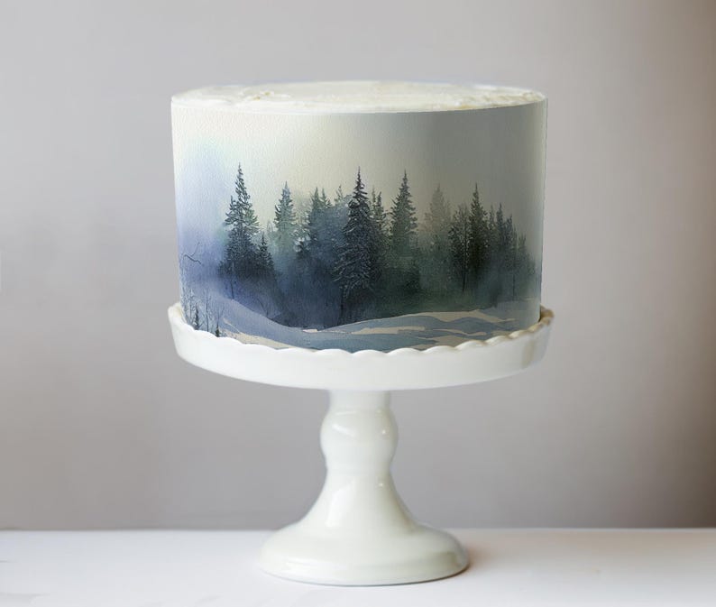 May include: A round cake with a forest scene design, displayed on a white, scalloped-edge cake stand. The cake features a watercolor-style painting of evergreen trees in shades of blue and green, creating a serene, natural aesthetic.