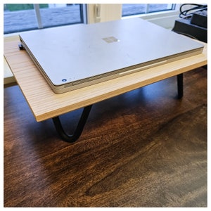 May include: A silver laptop computer is sitting on a wooden laptop stand with black metal legs. The stand is on a dark brown wooden surface.