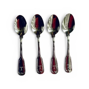 May include: Four silver spoons with a reflective surface are arranged in a row against a white background. Each spoon has a long handle and a bowl-shaped head. The handles have a decorative design and the letter "T" is engraved at the base.