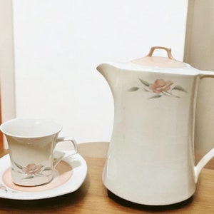 May include: A white ceramic teapot with a pink lid and floral design, along with a matching white teacup and saucer with a pink rim and floral design.