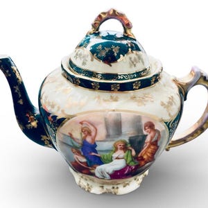 Könnte beinhalten: Eine antike Porzellan-Teekanne mit cremefarbenem Korpus, goldenen Akzenten und einem dunkelblauen Deckel und Ausguss. Die Teekanne zeigt eine gemalte Szene mit klassischen Figuren und einem goldenen Griff.