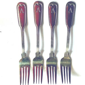 May include: Four antique forks with a silver finish. Each fork features a red handle with a silver heart-shaped design and a capital "A" in the center. The tines are silver and the forks are arranged on a white background.