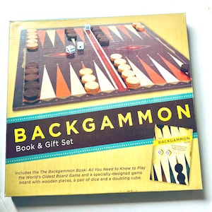 May include: A Backgammon book and gift set box featuring a dark brown board with orange and cream triangles, wooden playing pieces, two white dice, and a doubling cube. The text reads BACKGAMMON Book & Gift Set and includes a small book cover image.