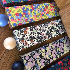 May include: A selection of rectangular boxes with floral designs in shades of blue, yellow, and black. The boxes are displayed on a wooden surface, accompanied by a few spherical decorative items.