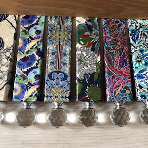 May include: A selection of decorative bottle stoppers. Each stopper features a patterned fabric top with a faceted crystal base. The fabric designs showcase floral and abstract patterns in blue, green, and red.