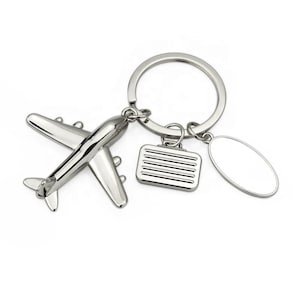 Peut inclure: Porte-clés en argent en forme d'avion avec une étiquette à bagages et un charme ovale vide. Le porte-clés est attaché à un anneau de clé en argent.