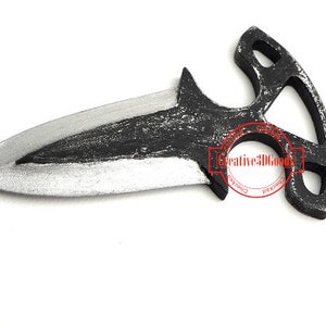 Puede incluir: Un cuchillo de lanzamiento de metal negro y plateado con un diseño de mango único. El mango tiene un agujero grande en el centro y dos agujeros más pequeños a cada lado. El cuchillo mide aproximadamente 15 cm de largo.