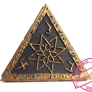 Może przedstawiać: Trójkątna drewniana tabliczka z pozłacanym ramą i gwiazdką w środku. Tabliczka ma ciemnobrązowe wykończenie drewna, a gwiazdka jest wykonana ze złotego metalu.