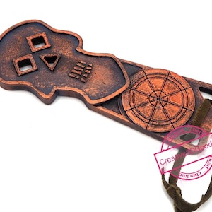 May include: A copper-coloured bottle opener shaped like a skull with a compass design. The skull has a triangle for a nose and two square eye sockets. The compass is surrounded by a circle with a rope loop.