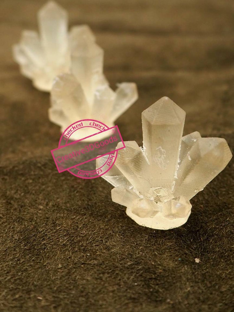 May include: Three clear crystal clusters of varying sizes, arranged in a row on a brown textured surface.