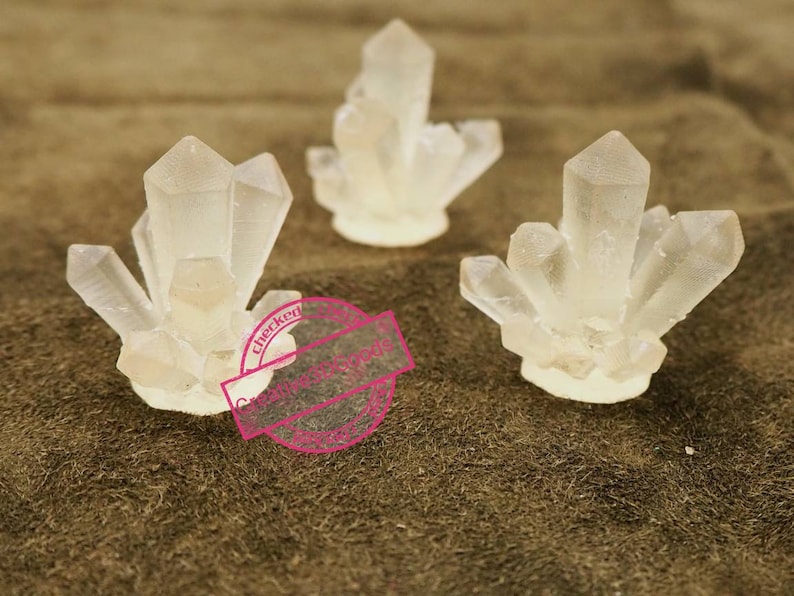 May include: Three clear crystal clusters, each with a different shape and size, are arranged on a brown surface. The crystals are made of clear resin and have a smooth, polished finish.