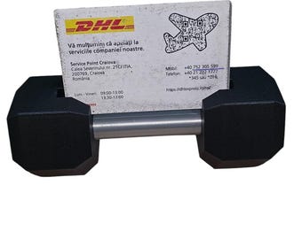 May include: A black dumbbell with a silver bar holding a white business card with the DHL logo and contact information for a service point in Craiova, Romania. The business card includes the address, phone number, mobile number, and website address. The text on the business card reads: "Vă mulțumim că apeiați la serviciile companiei noastre. Service Point Craiova Calea Severinului nr. 21C/ITIA 200769, Craiova România Luni-Vineri: 09:00-13:00 13:30-17:00 Mobil: +40 752 305 599 Telefon: +40 21 222 1777 *345 sau DHL https://dhlexpress.ro/tel"
