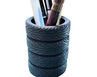 May include: A black tire-shaped pen holder with a white pen, a black pen, and a red pen inside.