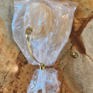 May include: A decorative, clear glass object with a gold-colored metal accent, wrapped in clear plastic. The object has a curved stem and a small, round gold-colored accent piece. The item is packaged in a clear plastic bag.