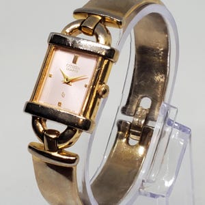 May include: A gold-tone Citizen Quartz wristwatch with a square face and a bangle-style band.