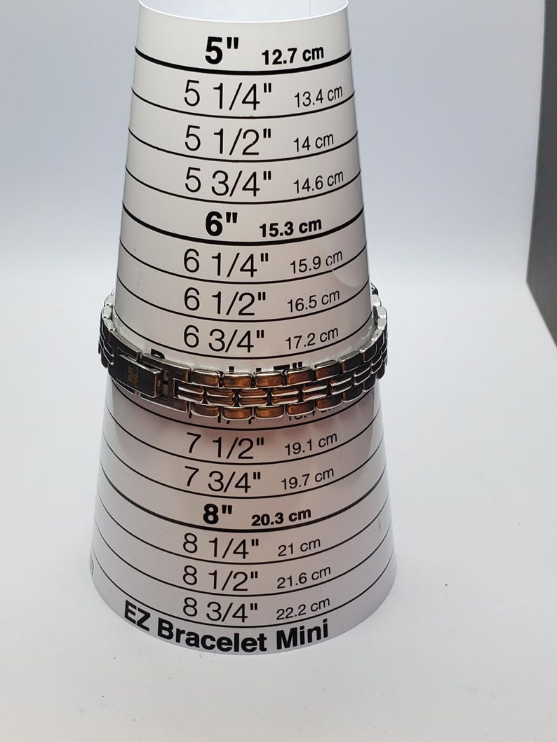 Puede incluir: Una pulsera plateada y marr&oacute;n se coloca en una herramienta de medici&oacute;n EZ Bracelet Mini. La herramienta mide de 12,7 cm a 22,2 cm. La pulsera est&aacute; hecha de eslabones rectangulares.