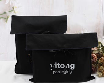 Könnte beinhalten: Zwei schwarze Stoffbeutel mit Überschlag und Kordelverschluss. Auf den Beuteln steht in Weiß "yitong packaging". Die Beutel werden auf einer weißen Oberfläche präsentiert.