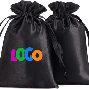 Puede incluir: Dos bolsas de cordón de satén negro con cordones negros. Una bolsa tiene la palabra "LOGO" impresa en letras de colores.