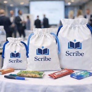 May include: Three white drawstring bags with blue drawstrings, each printed with the "Scribe" logo and a blue book icon. The bags are on a white tablecloth with snacks, a pen, and water bottles. A conference is in the background.