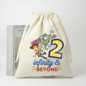 Könnte beinhalten: Beige Kordelzugbeutel mit farbenfroher Grafik von Buzz Lightyear und Woody aus Toy Story, der Zahl 2 und dem Schriftzug "infinity & beyond". Wahrscheinlich für einen Kindergeburtstag.