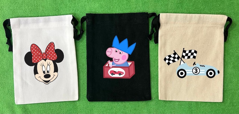 May include: Three drawstring bags with different designs. The first bag is white with a red and white polka dot bow and a black and white cartoon mouse face. The second bag is black with a pink pig wearing a blue crown and holding a red toy car. The third bag is beige with a blue race car with a checkered flag and the number 3 on the side.