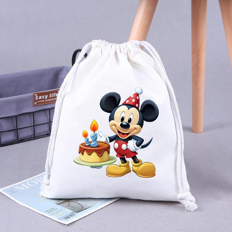 May include: White drawstring bag with a cartoon image of Mickey Mouse holding a birthday cake with candles. The bag has a red and white polka dot pattern.
