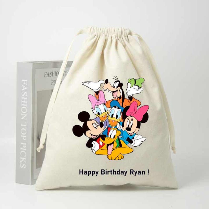 May include: A white cotton drawstring bag with a colorful print of Mickey Mouse, Minnie Mouse, Donald Duck, Goofy, Pluto, and Daisy Duck. The bag has the text "Happy Birthday Ryan!" printed on the front.