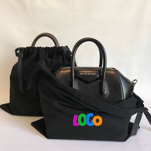 Pode incluir: Bolsa de mão de couro preto com um logotipo prateado que diz "Givenchy". A bolsa de mão está em uma bolsa de pó preta com um "LOGO" colorido impresso nela.