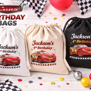 May include: Three drawstring birthday bags in white, tan, and black, each featuring a red race car graphic and the text "Jackson's 4th Birthday." The bags are decorated with race-themed elements.